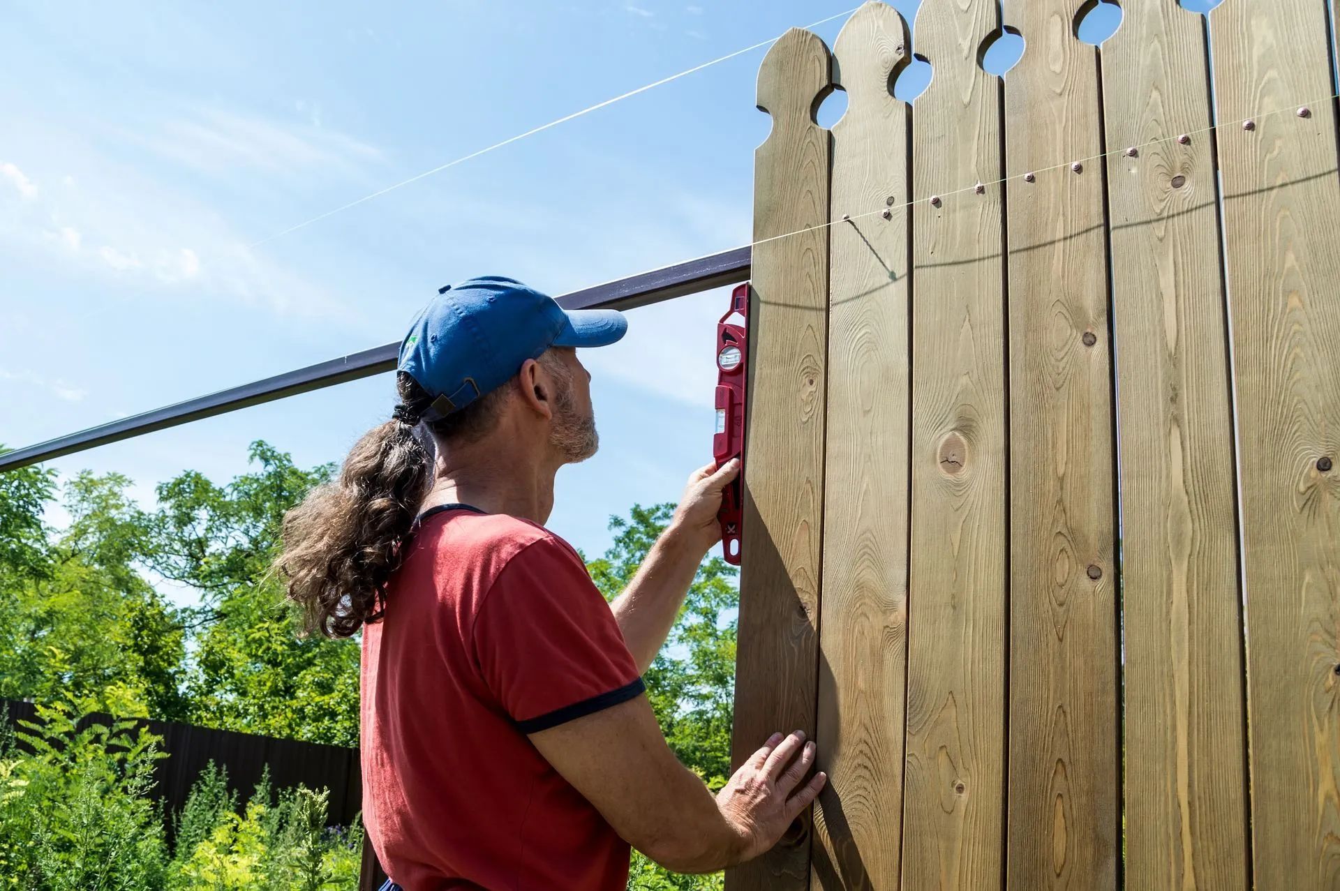 A man is measuring a wooden fence with a level.