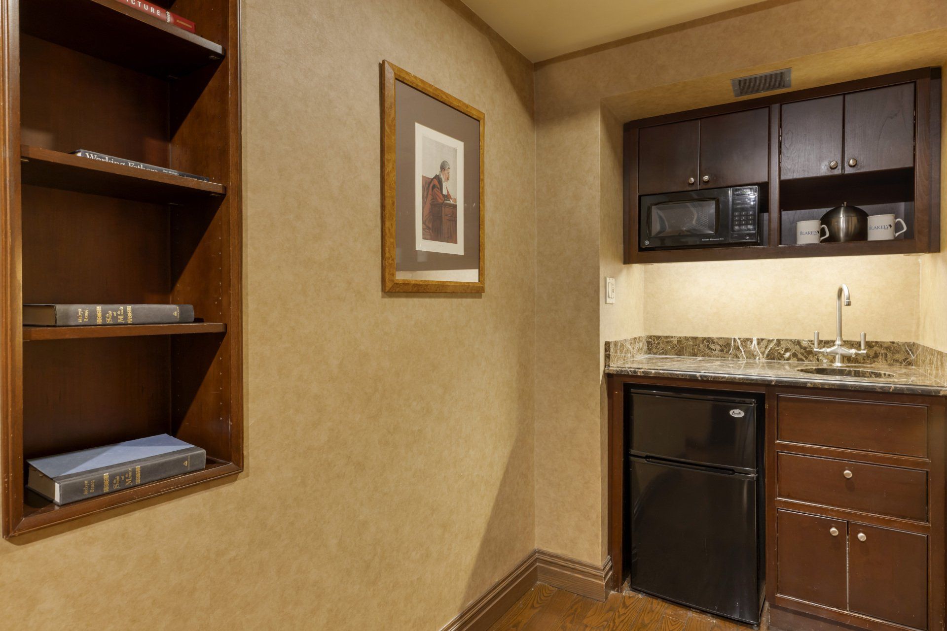 A small kitchen with a refrigerator , sink , microwave and bookshelf.