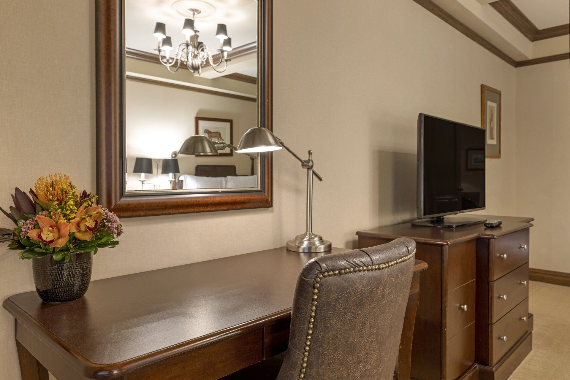 A hotel room with a desk , chair , television and mirror