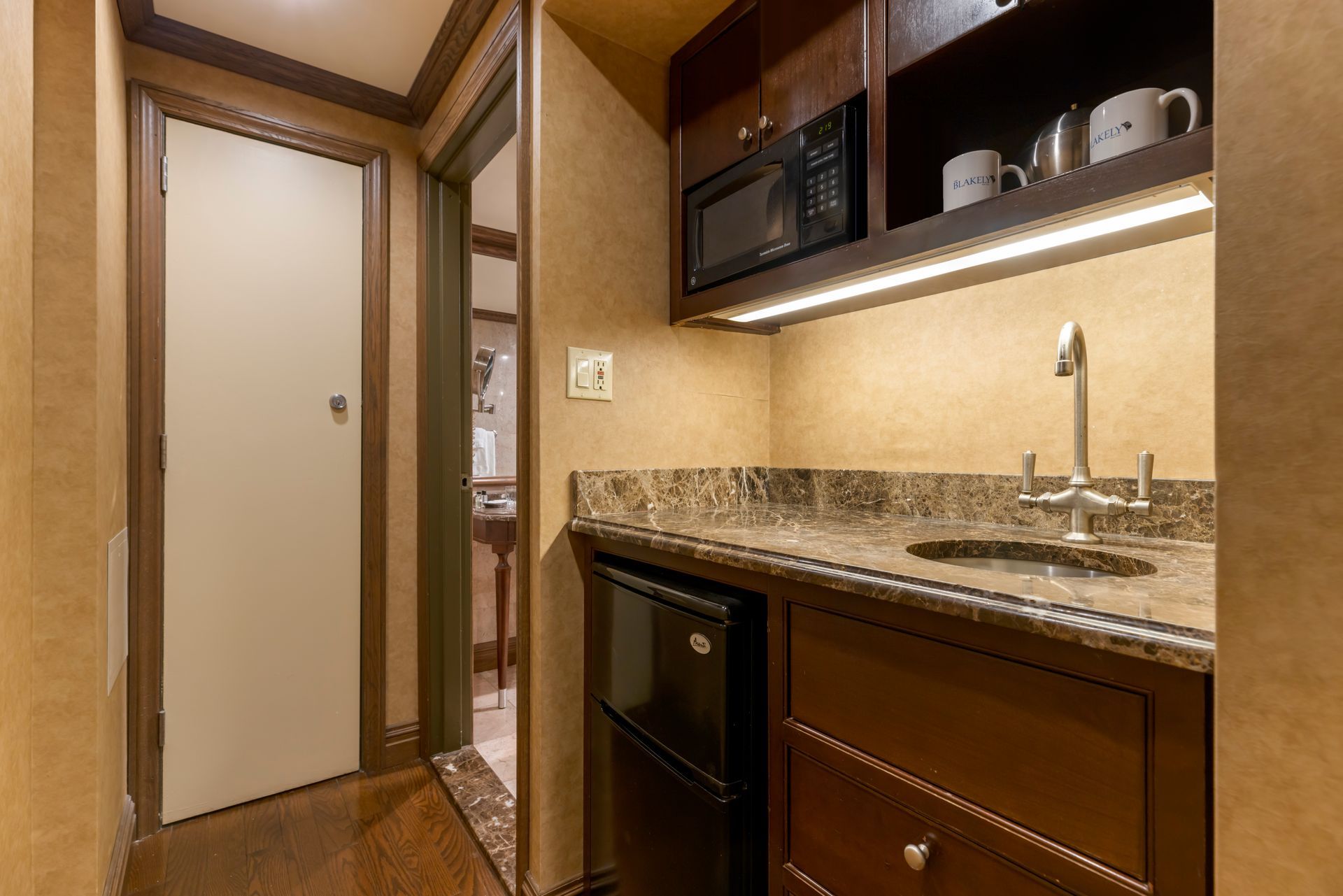 A small kitchen in a hotel room with a sink , microwave and refrigerator.