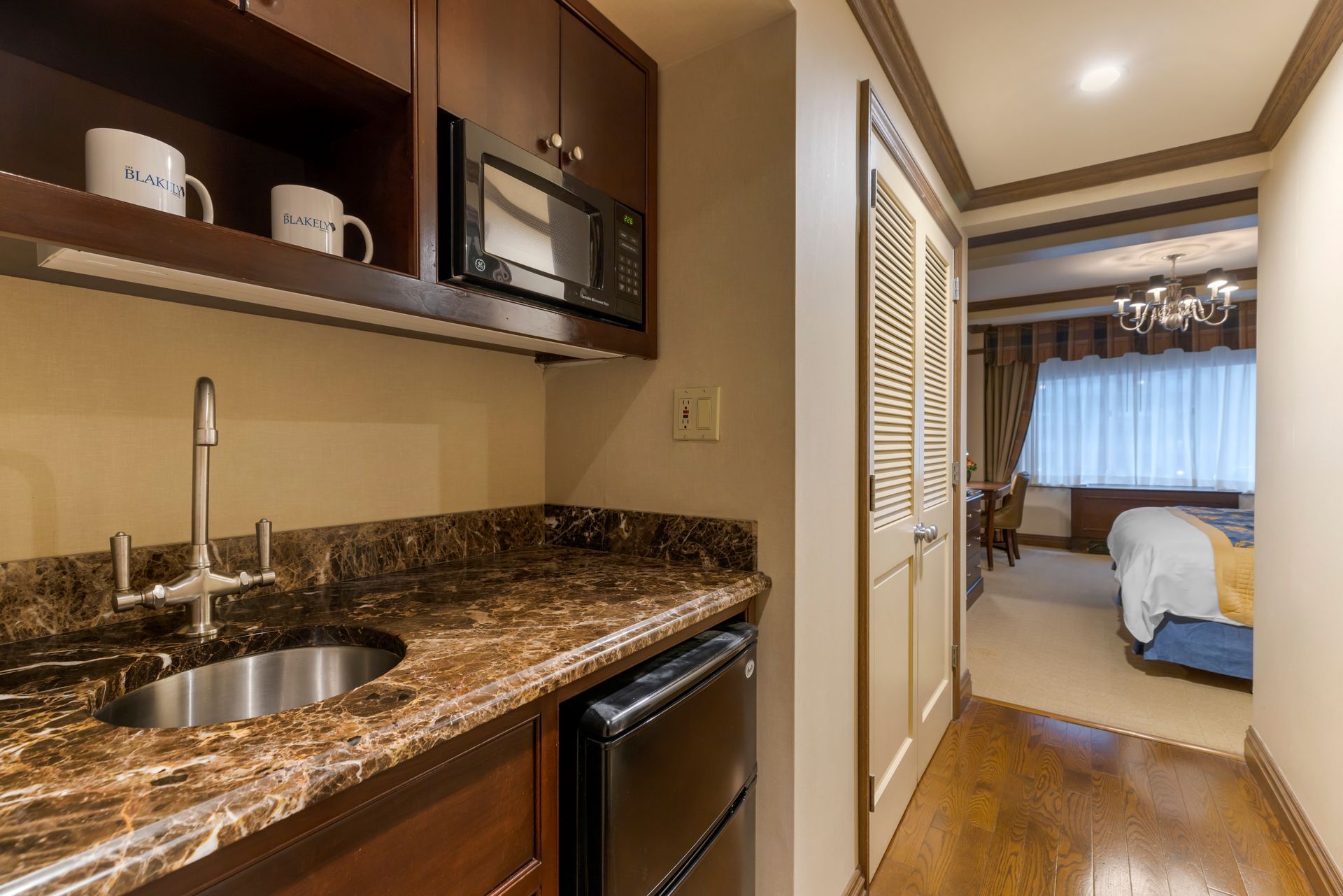 A hotel room with a kitchen with a sink , microwave and refrigerator.