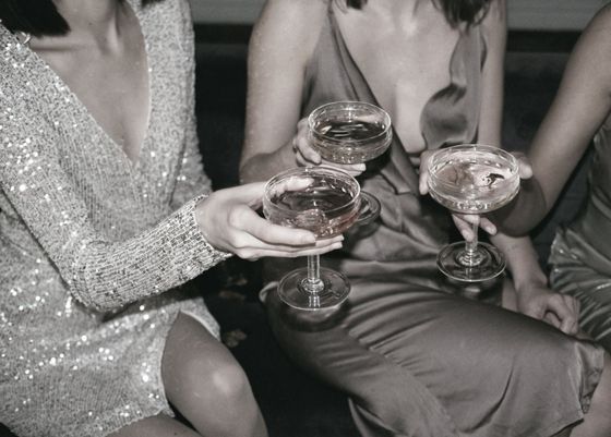 Three women are sitting on a couch holding champagne glasses.