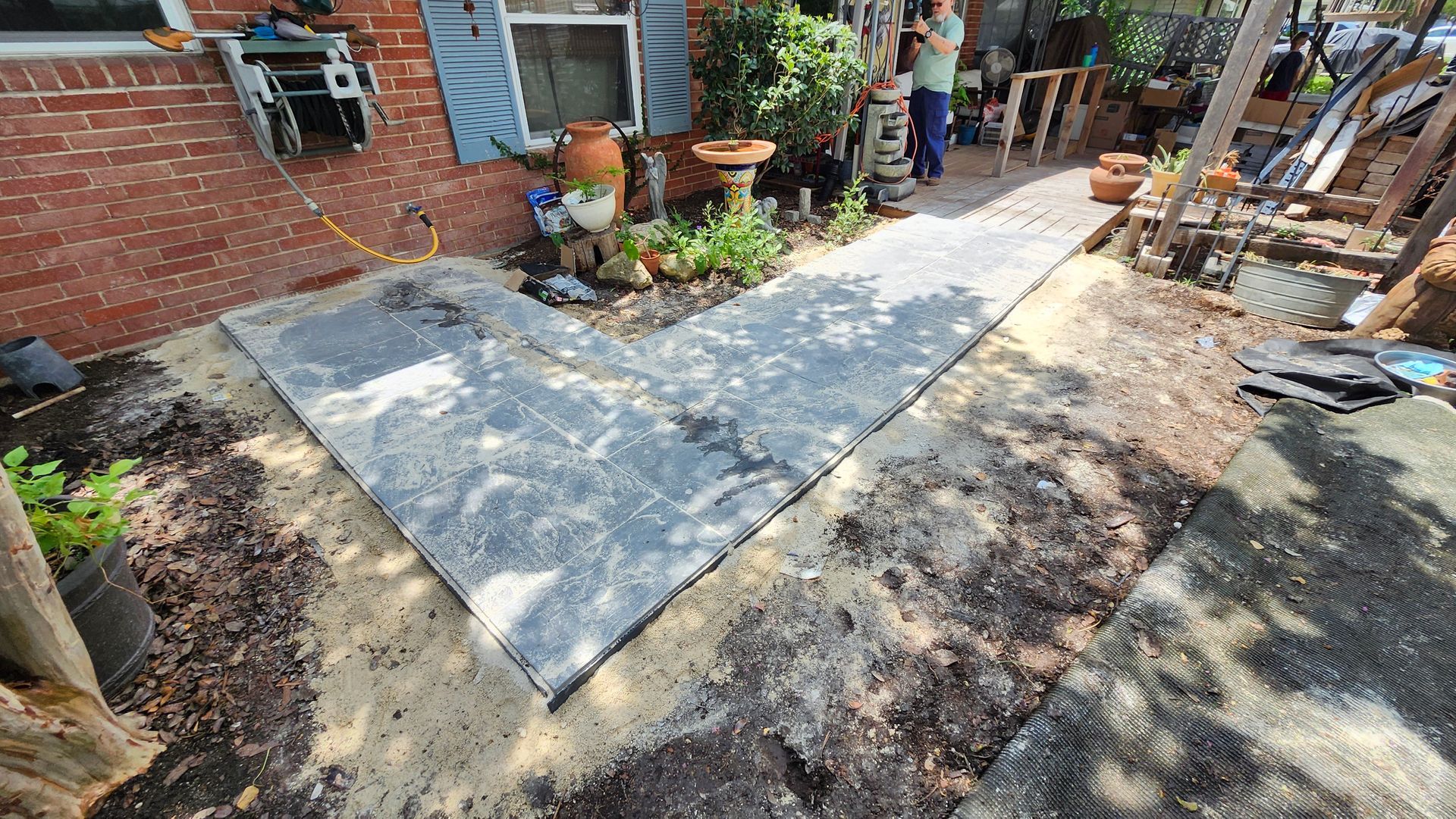 A pathway of concrete slabs leading to a building's entrance, surrounded by gravel, soil, and plants.