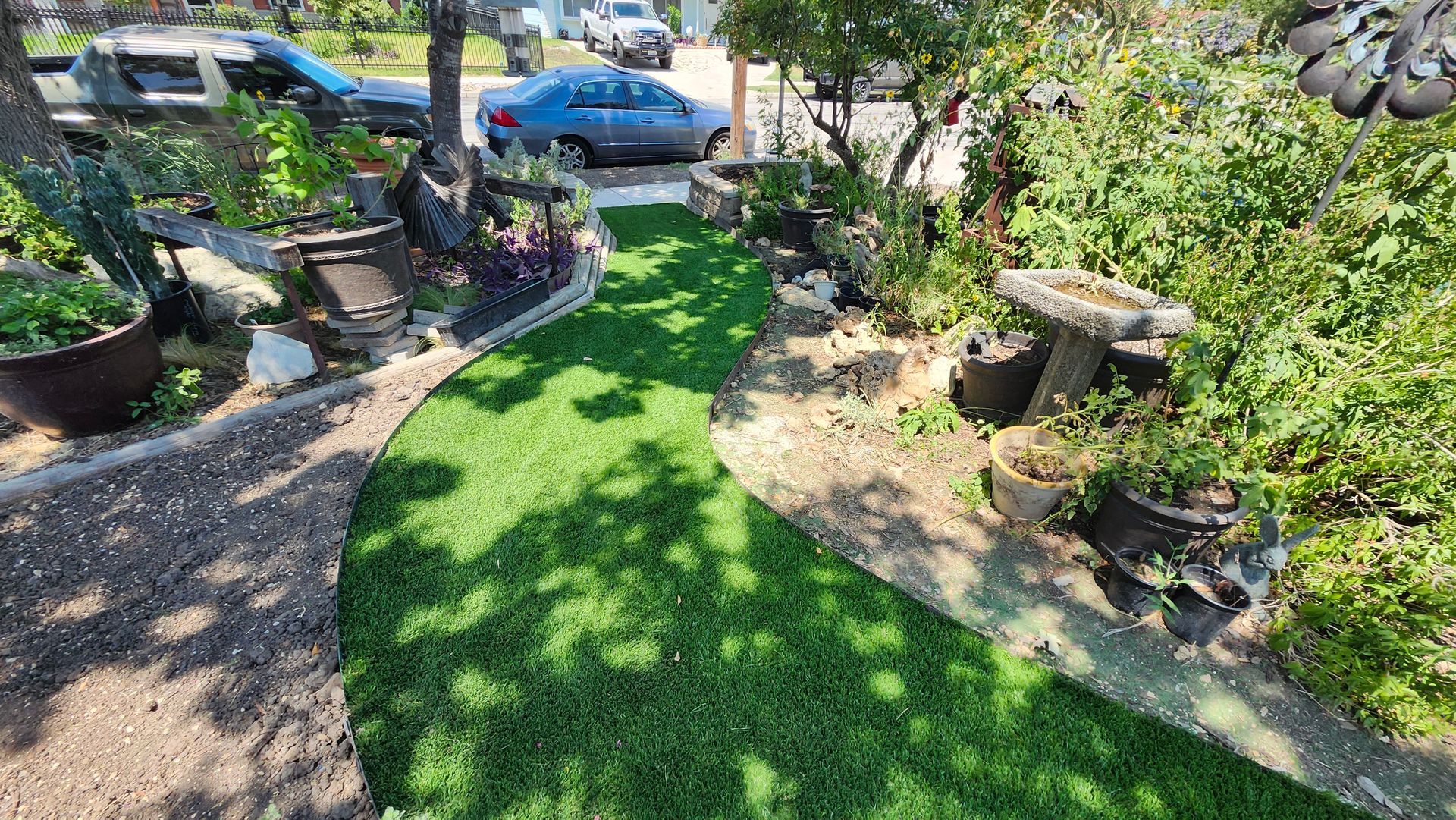 A winding path of green turf bordered by potted plants and greenery.