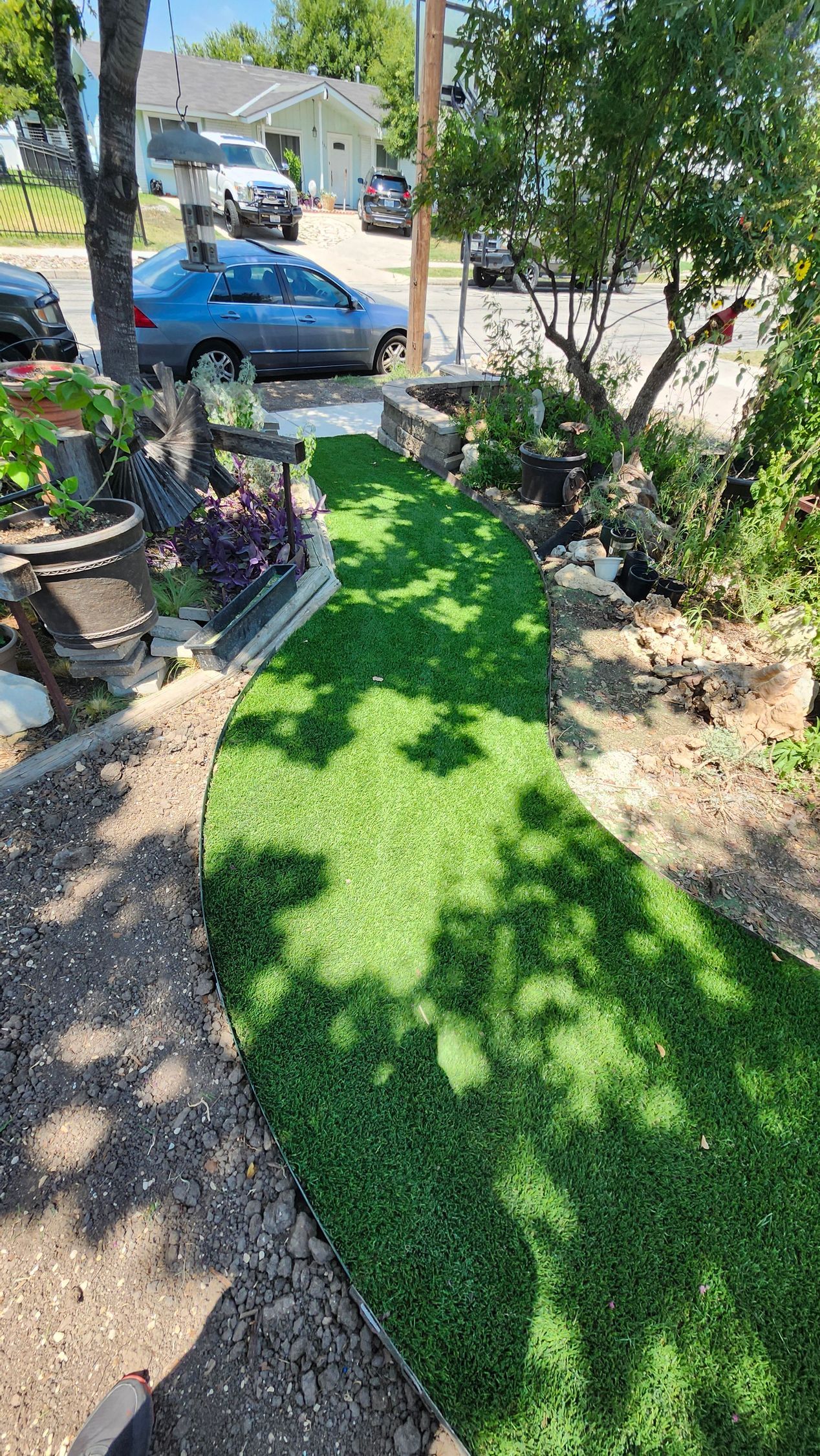 Artificial turf pathway leading to a street. Cars, trees, and landscaping surround the path.