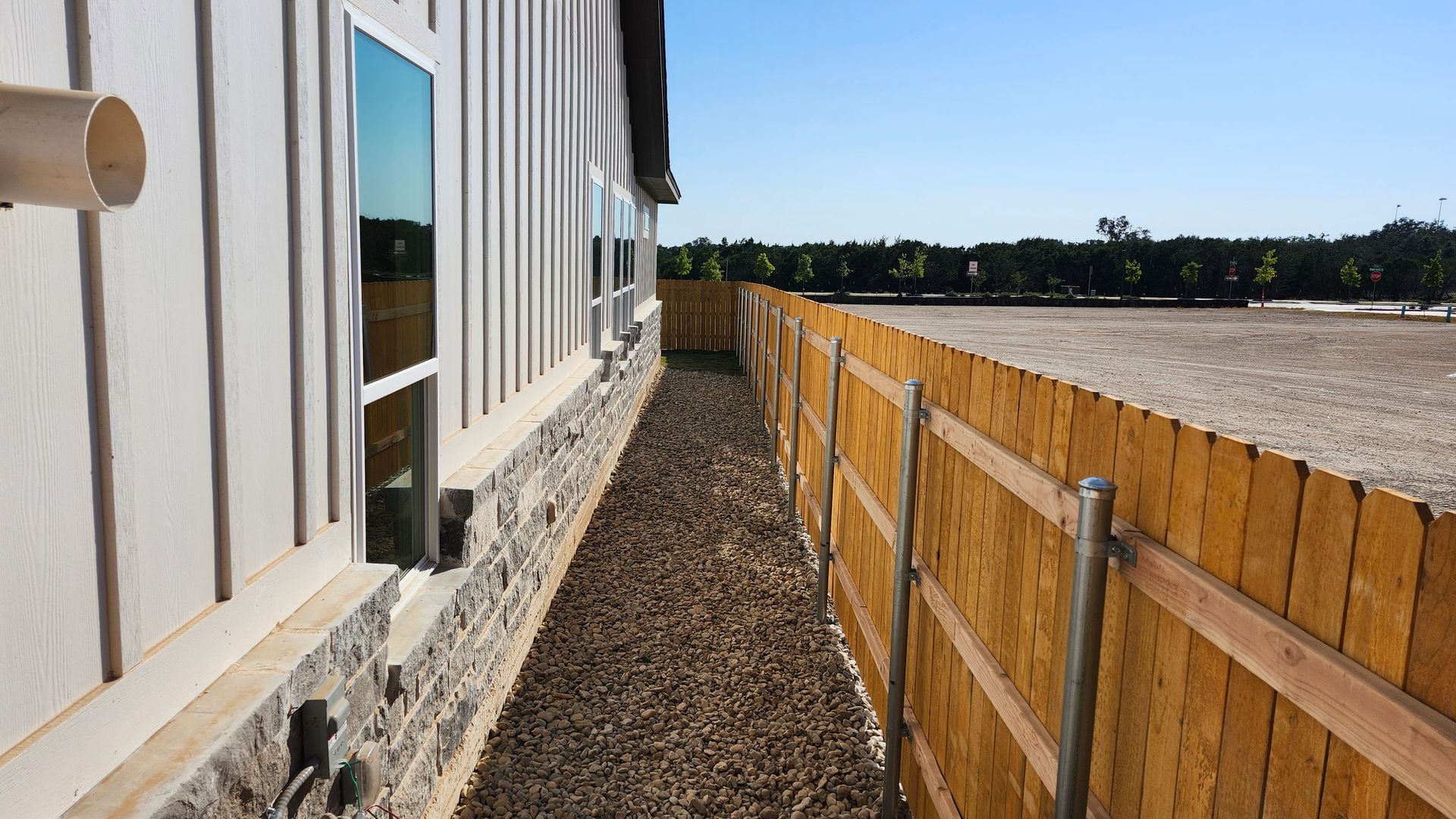 Side of a house with white siding and a gravel walkway next to a wooden fence.