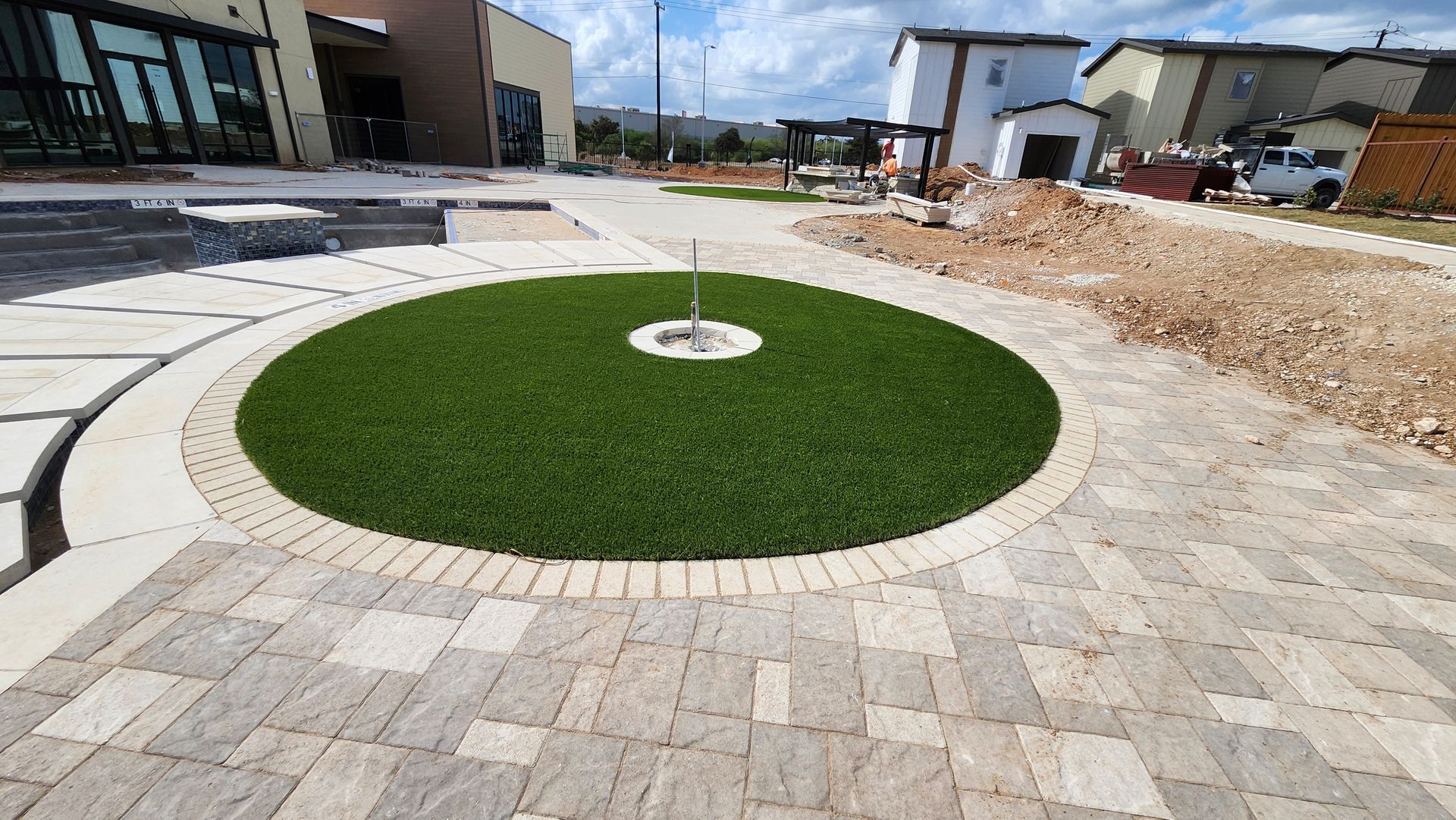 Circular lawn in a paved courtyard with a house in the background.