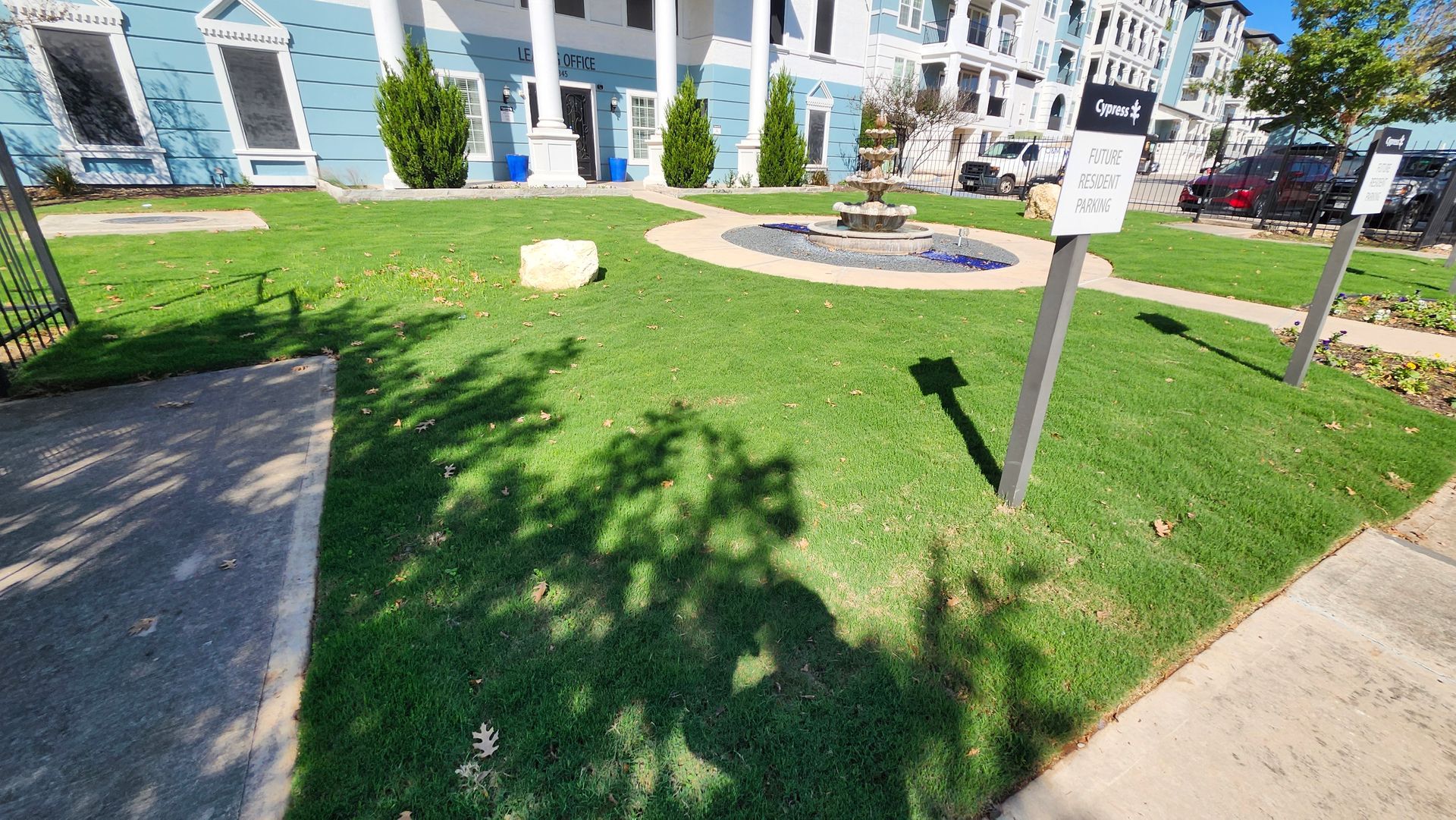 Green lawn with shadows, signs, and a building with blue facade.