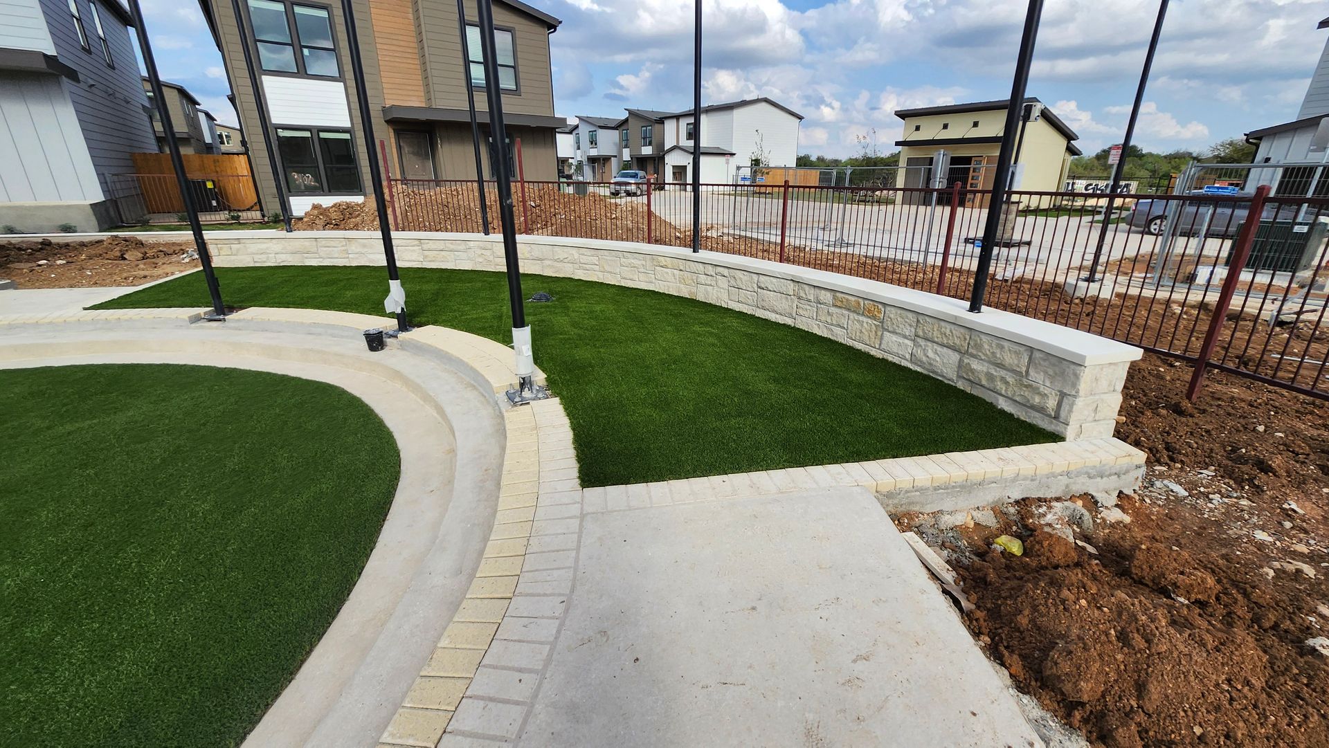A landscaped yard with artificial turf, stone walls, and a paved walkway.