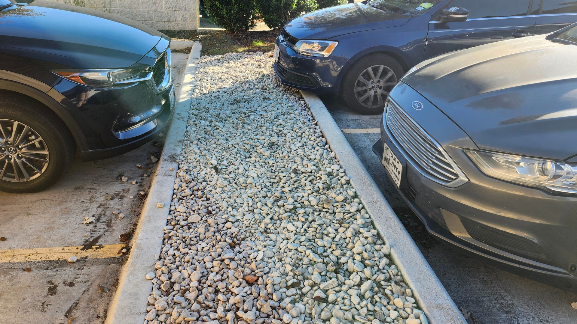 Cars parked on either side of a gravel-filled strip, bordered by concrete.