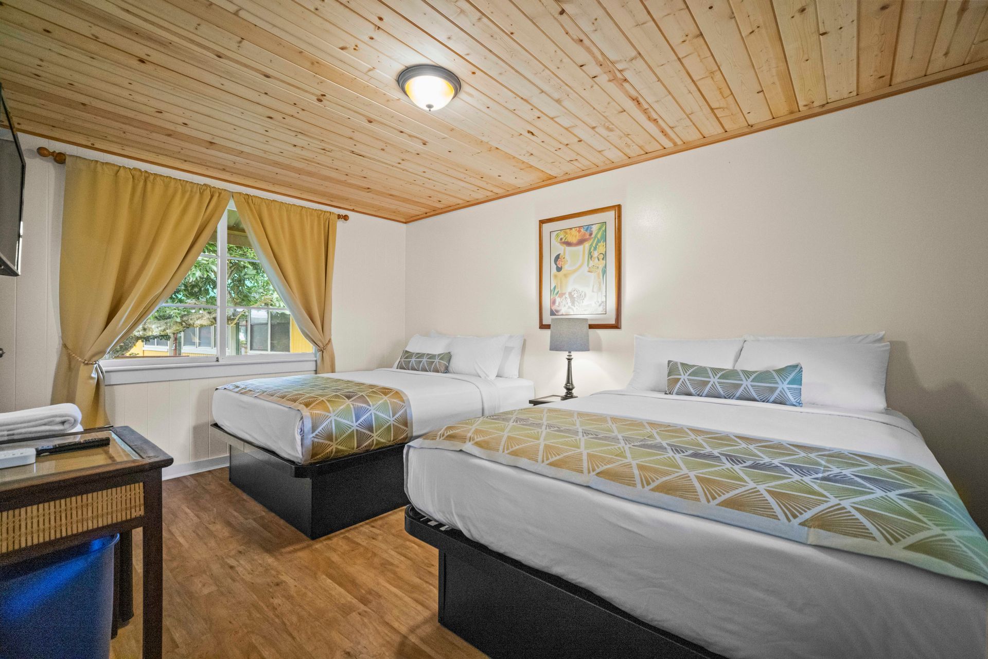 A hotel room with two beds, a wooden ceiling, and a window with yellow curtains.