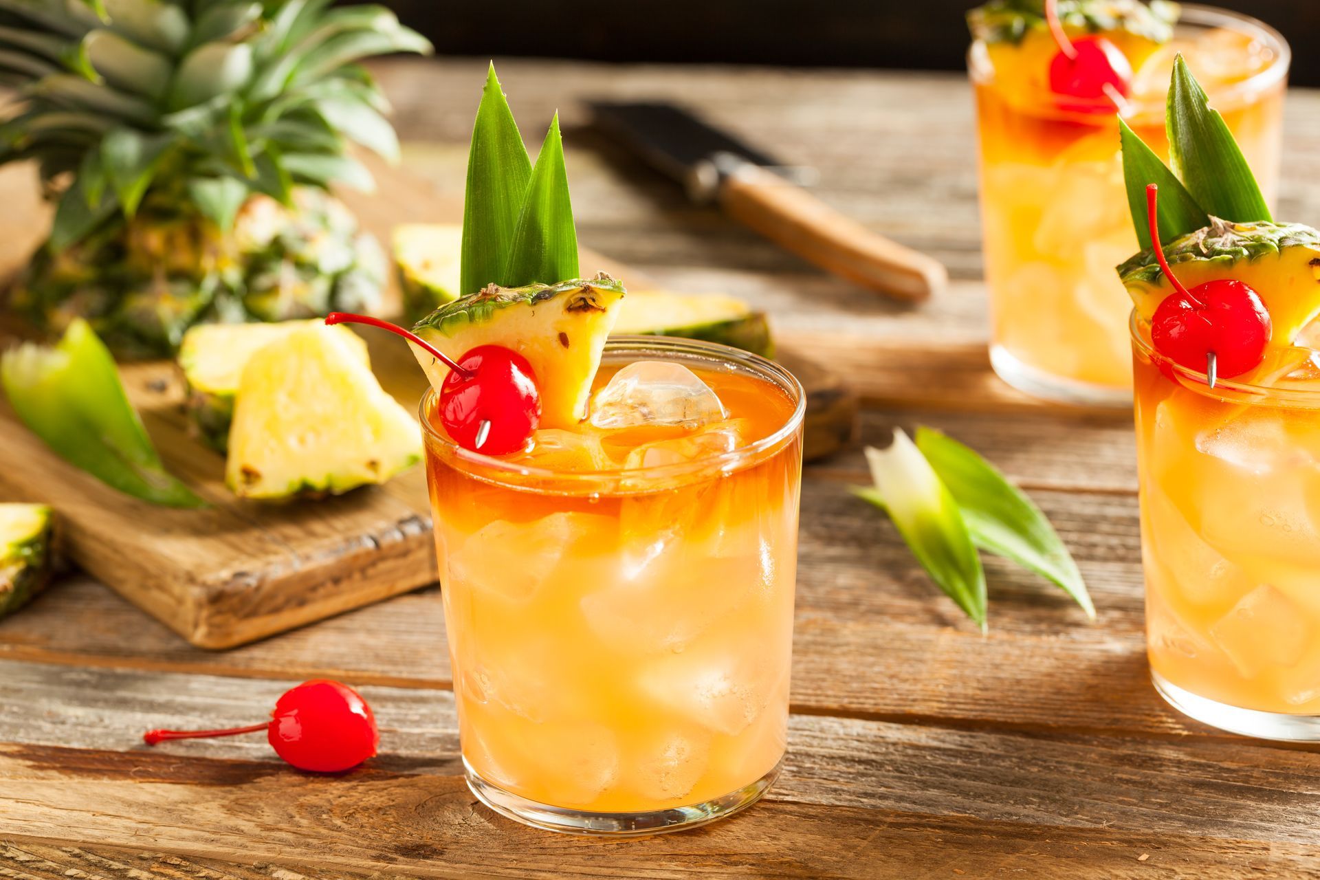 A close up of a pineapple and cherry cocktail on a wooden table.