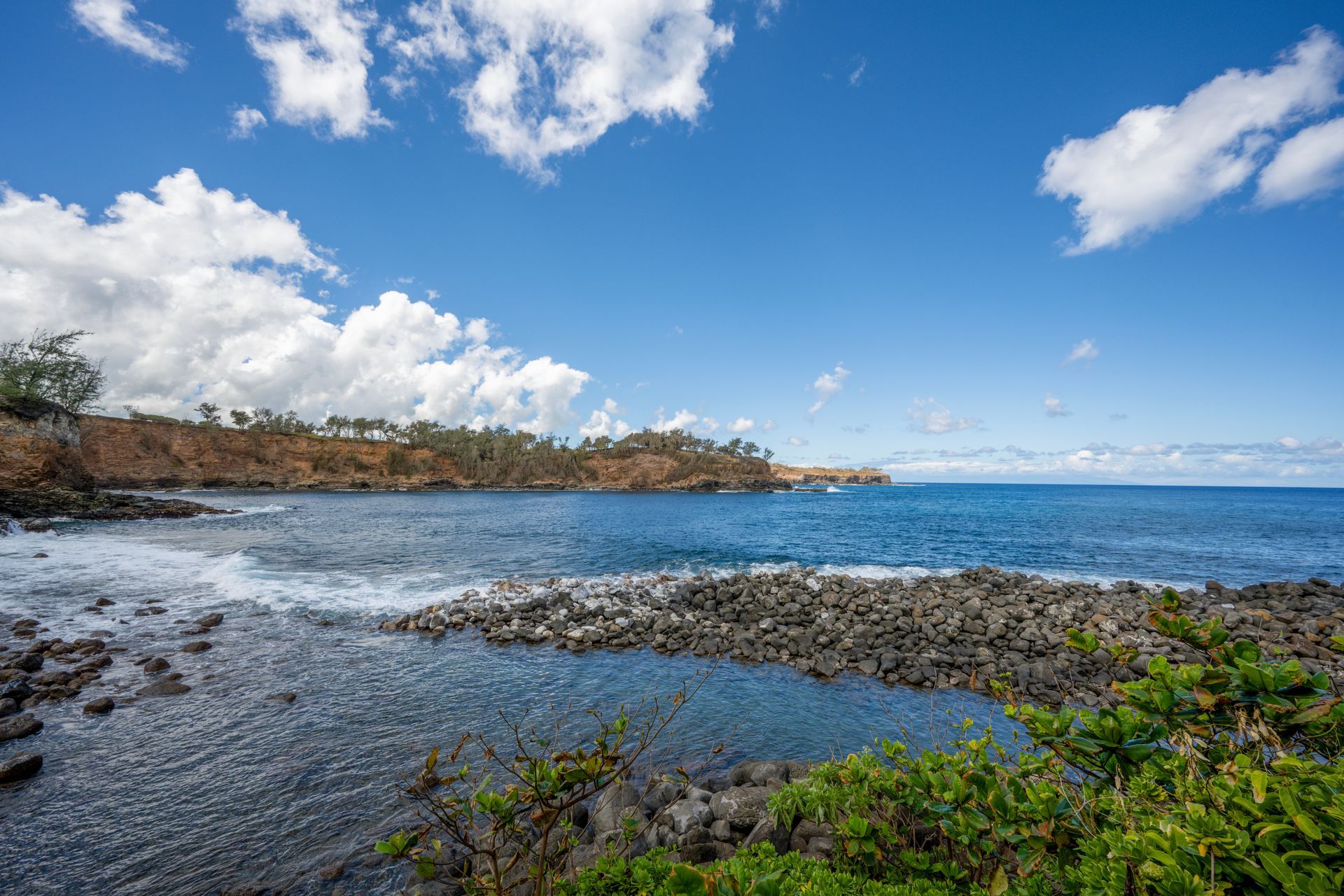 Rocky shoreline, blue ocean under a partly cloudy sky.