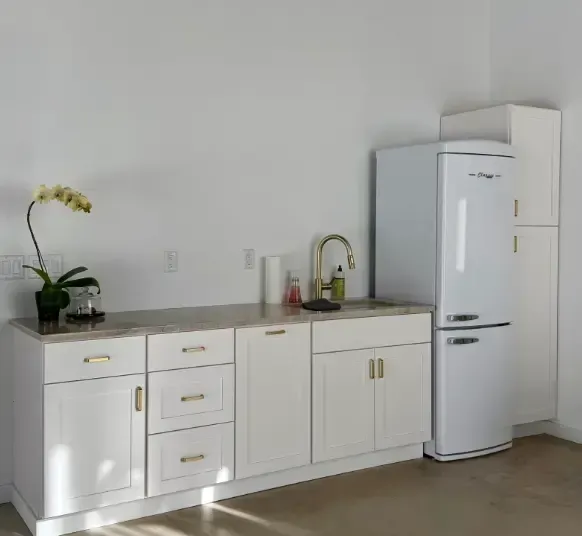 White kitchen cabinets with a gold faucet and a white retro-style refrigerator.