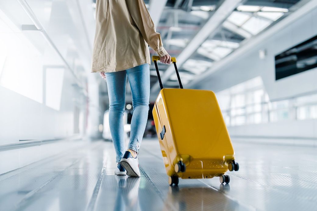 Una mujer camina con una maleta amarilla en un aeropuerto.