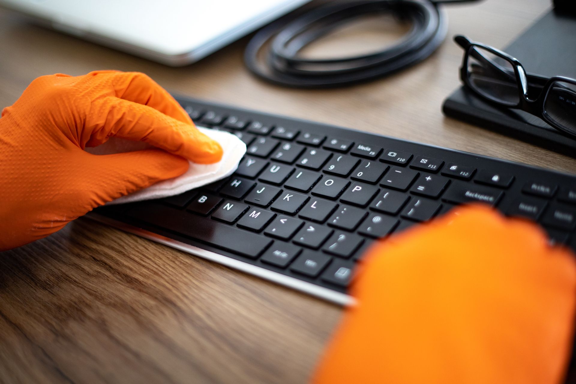 A person wearing orange gloves is cleaning a keyboard with a cloth.