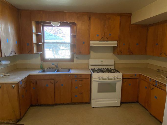 A kitchen with wooden cabinets , a stove , a sink and a window.