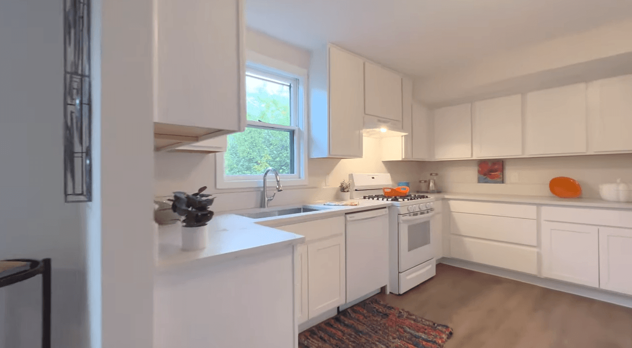 A kitchen with white cabinets , a stove , a sink , and a window.