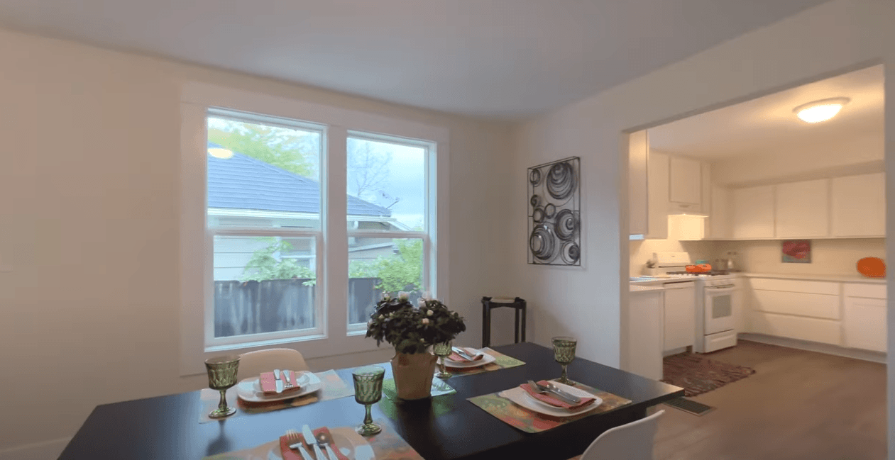 A dining room with a table and chairs and a kitchen in the background.