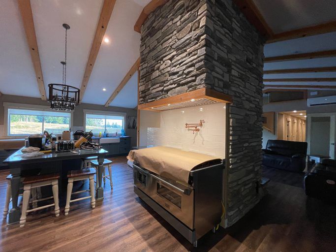 A kitchen with a stone wall and a stove in the middle of the room.