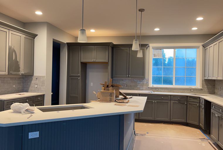 A kitchen with gray cabinets and white counter tops is being remodeled.