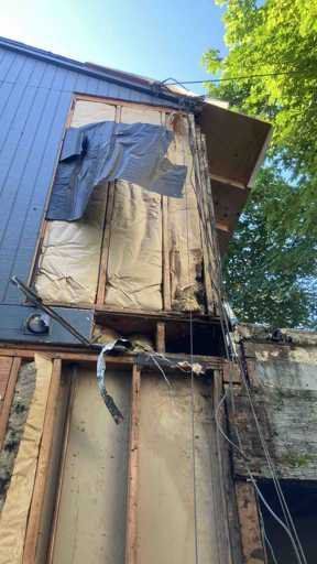 A house is being demolished and a tarp is hanging from the roof.