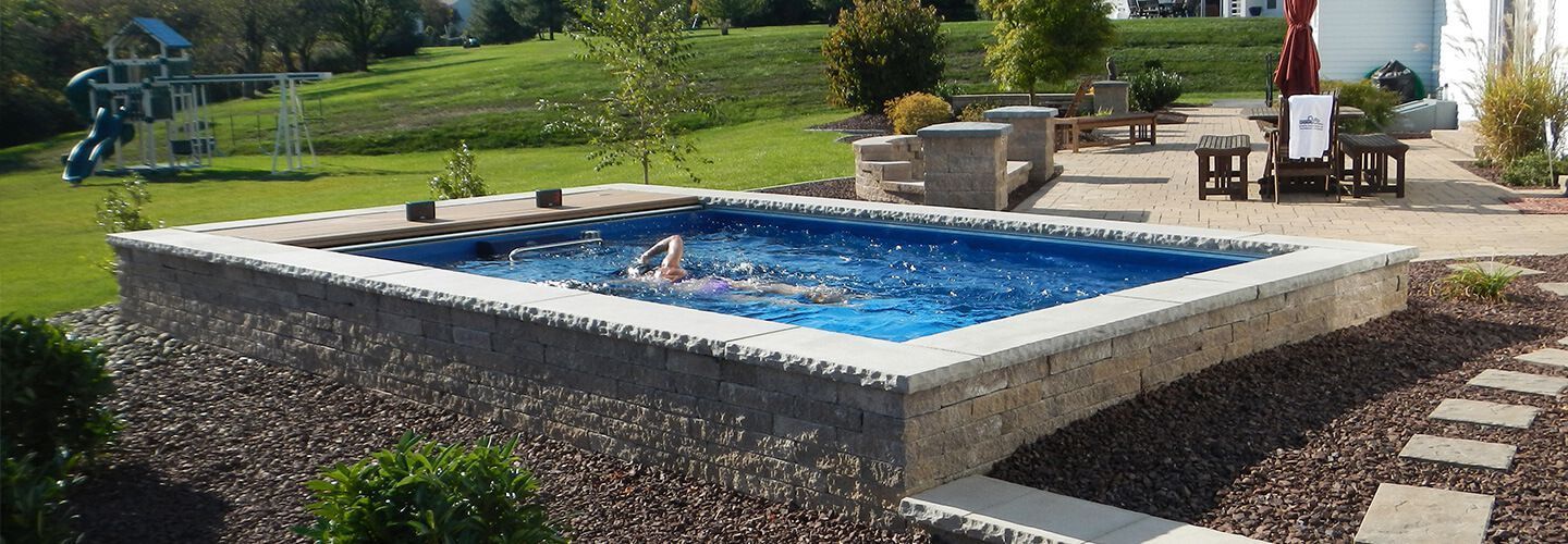 A person is swimming in a small swimming pool in a backyard.