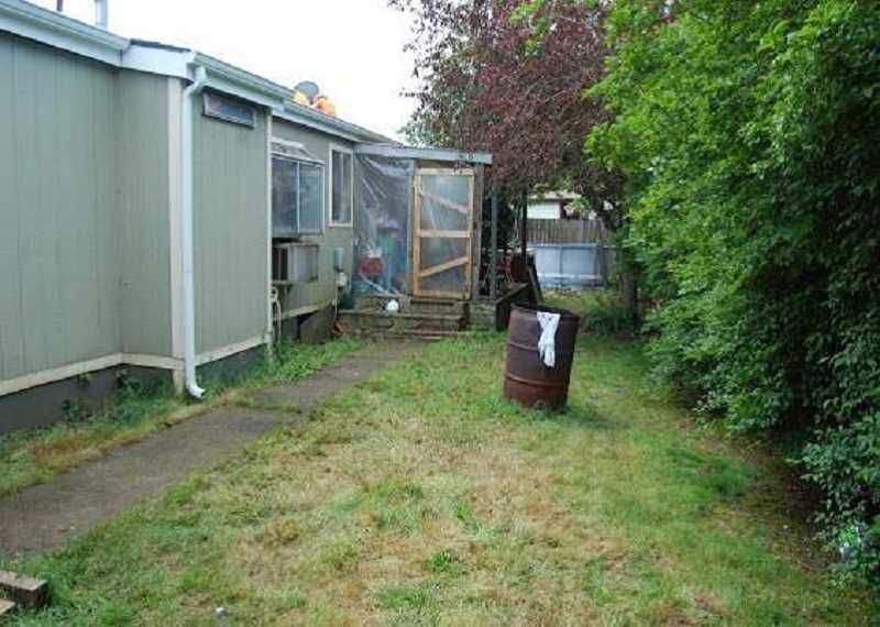 A backyard with a barrel in the middle of it and a house in the background.