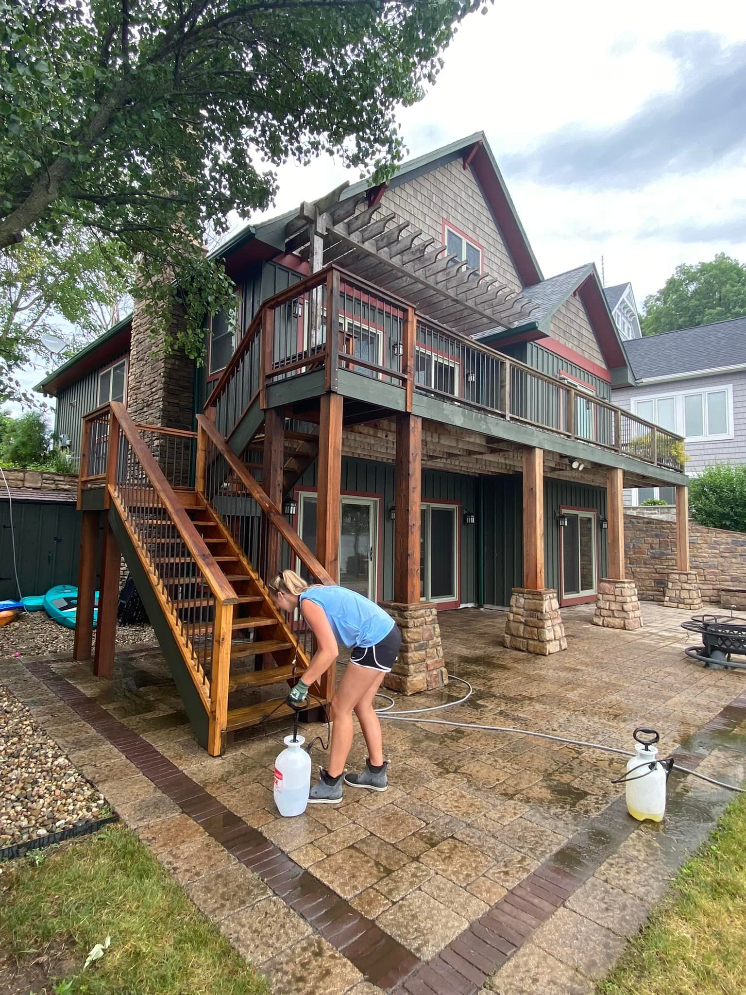 Woman cleaning wooden steps and patio of a multi-level house with a deck.