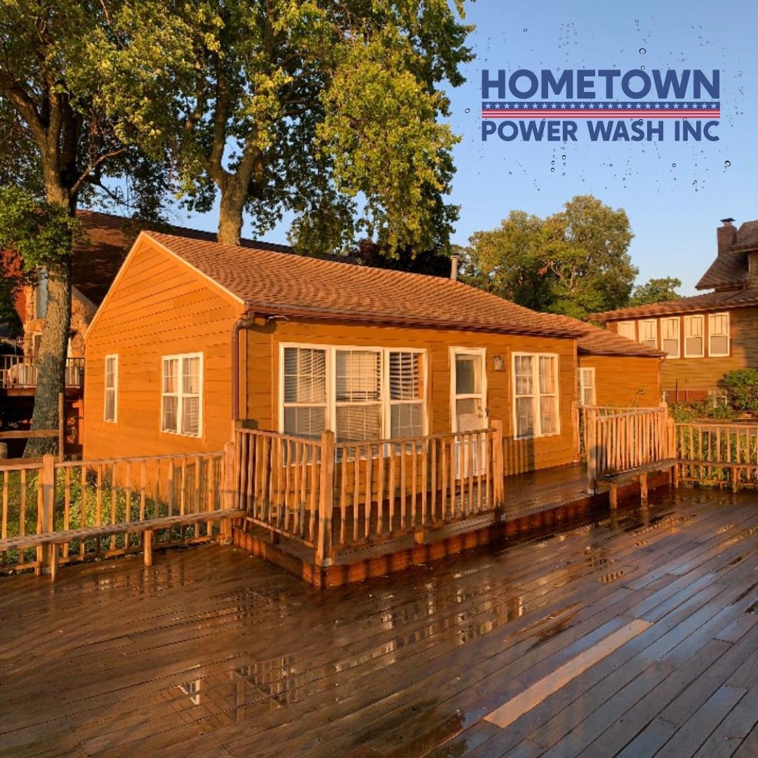 A cabin with wooden siding and a deck is being power washed, with a logo for Hometown Power Wash Inc. in the corner.