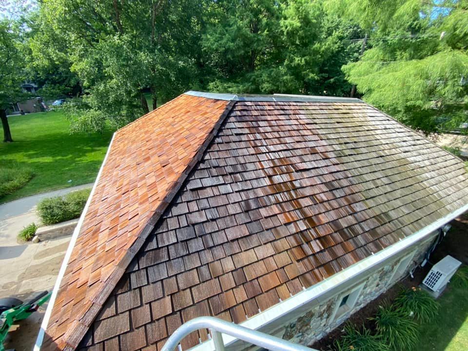 Half-cleaned cedar shake roof; half is stained and dirty, other half is clean and reddish-brown.
