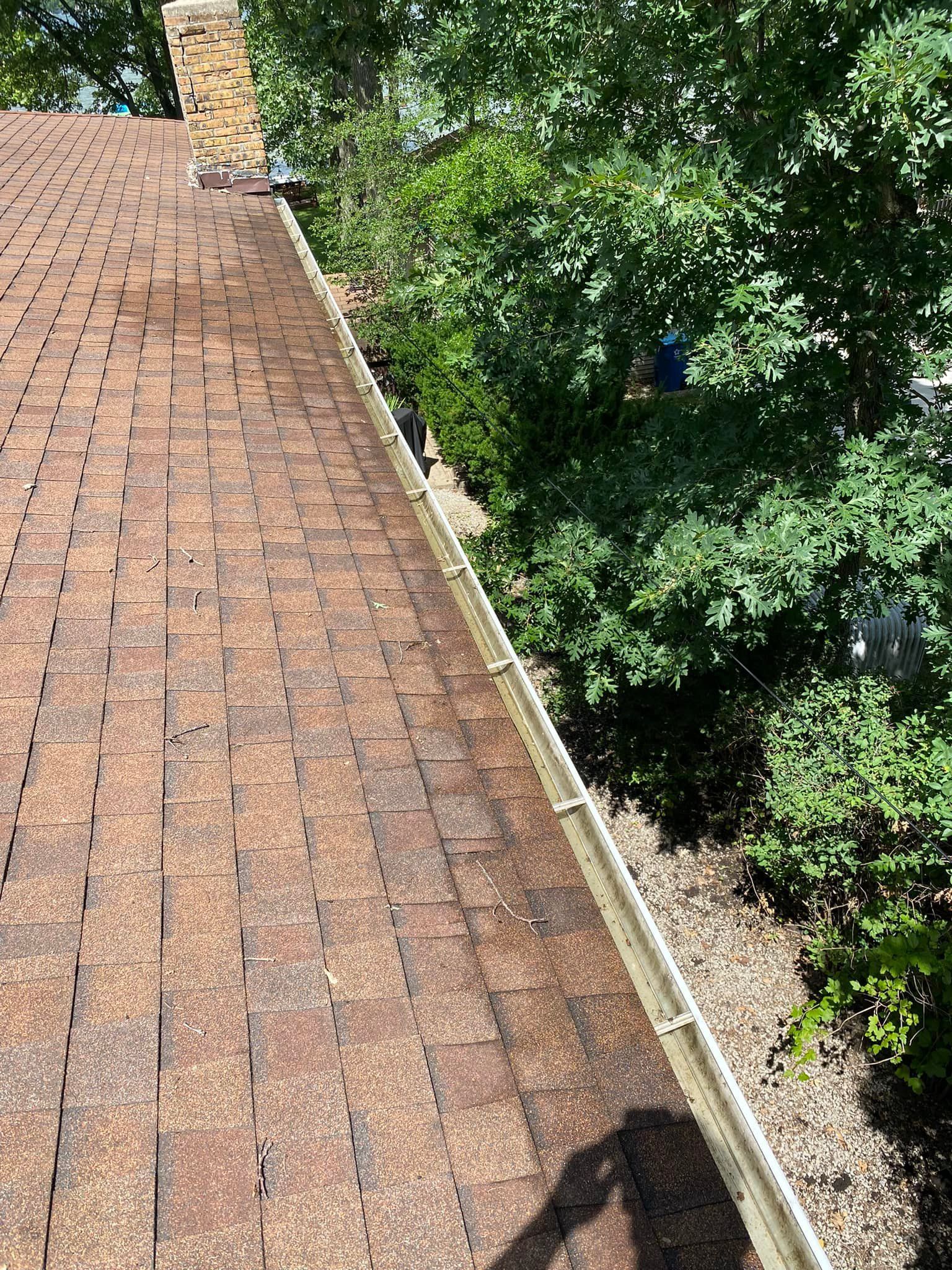 Brown shingled roof with a gutter, trees, and a chimney.