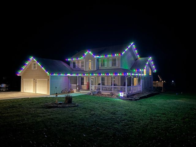 A house at night outlined with glowing blue and green Christmas lights, with illuminated garage doors and porch.