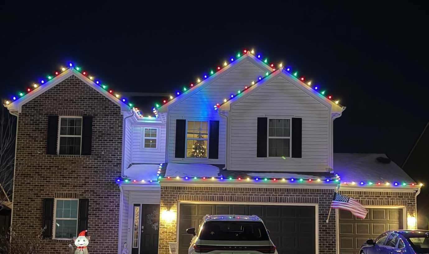 House with Christmas lights on roof, in front of a night sky.