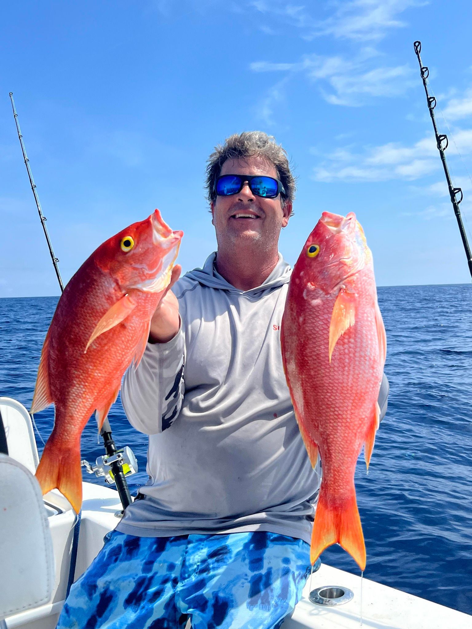 A man is holding two red fish on a boat in the ocean.