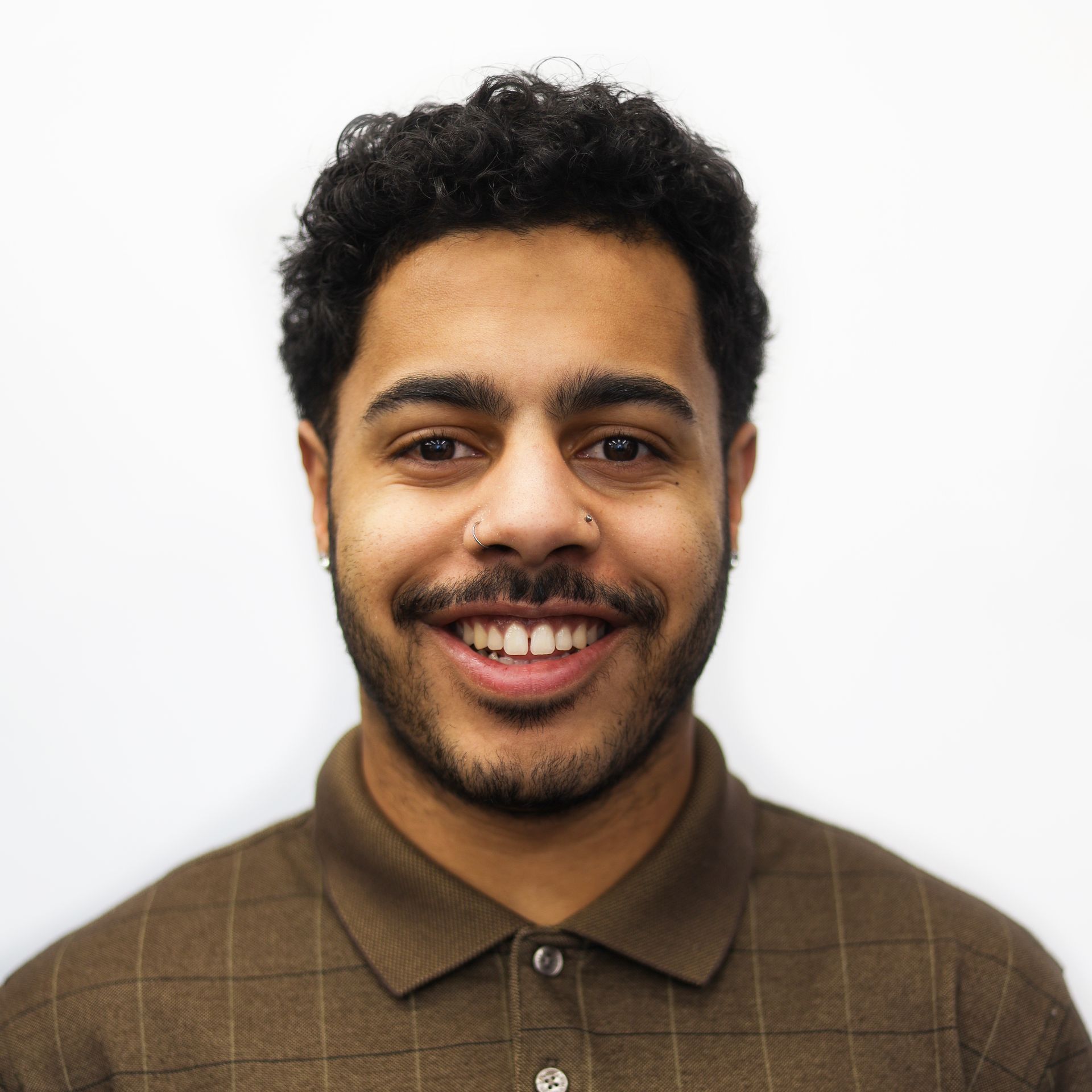 A man with a beard is smiling and wearing a brown shirt