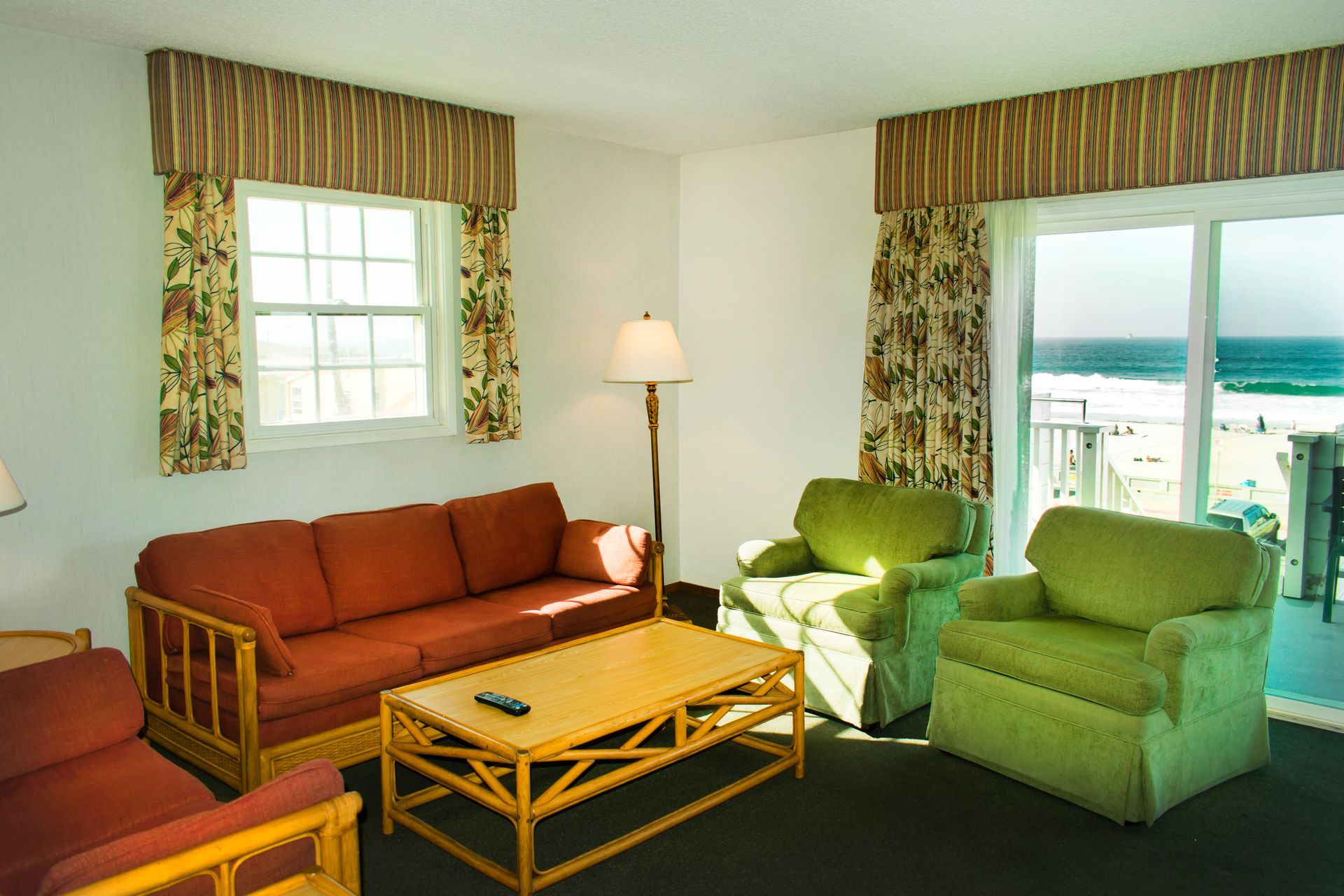 Living room with orange sofa, green armchairs, wooden table, and ocean view from a balcony.