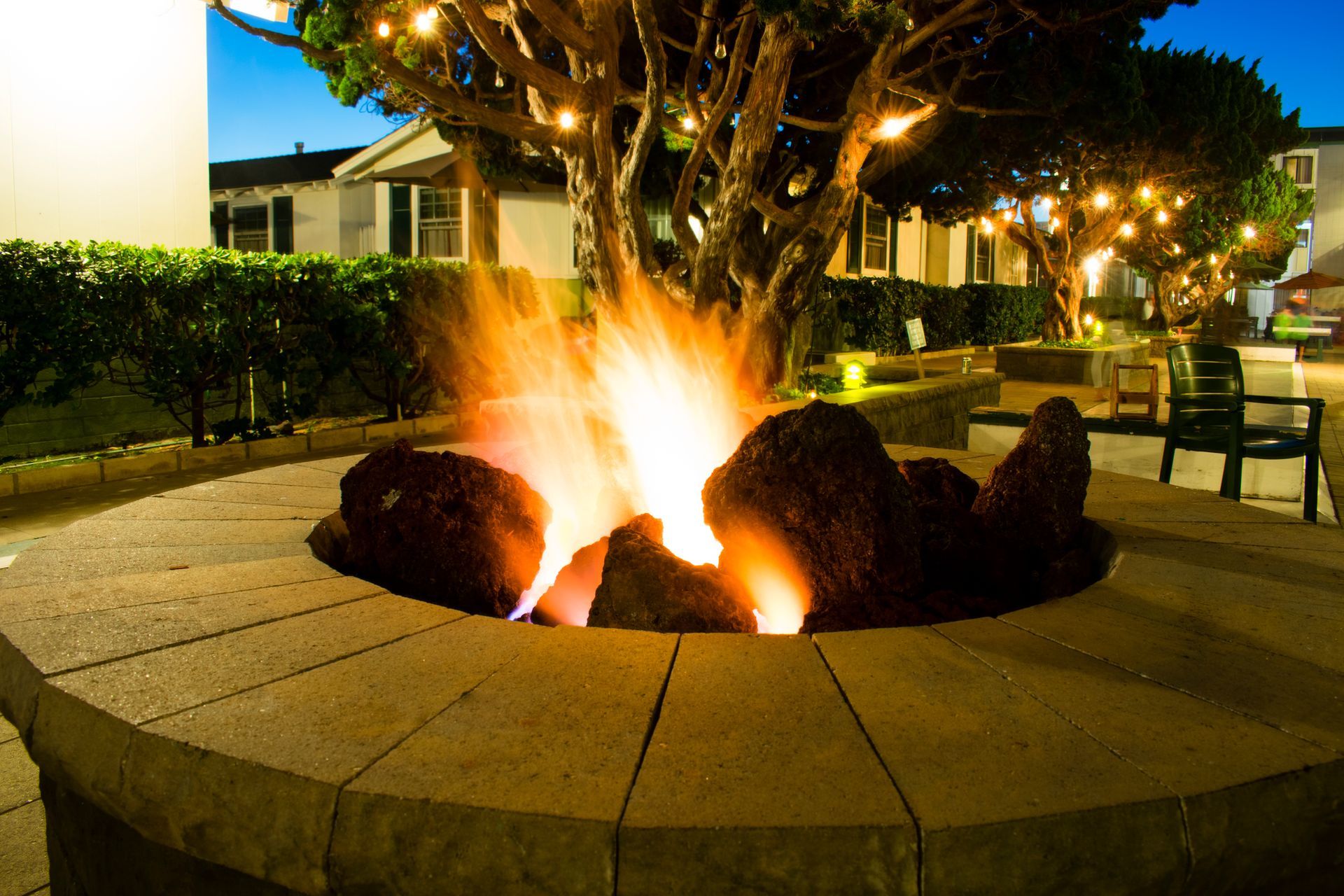 A lit fire pit surrounded by stone seating, with trees overhead strung with lights.