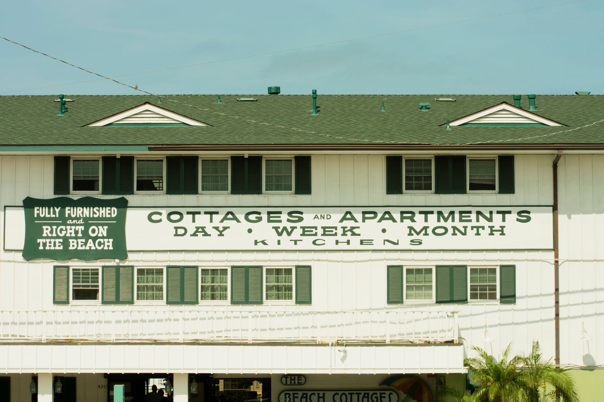 White hotel building with green shutters and roof, sign reading 
