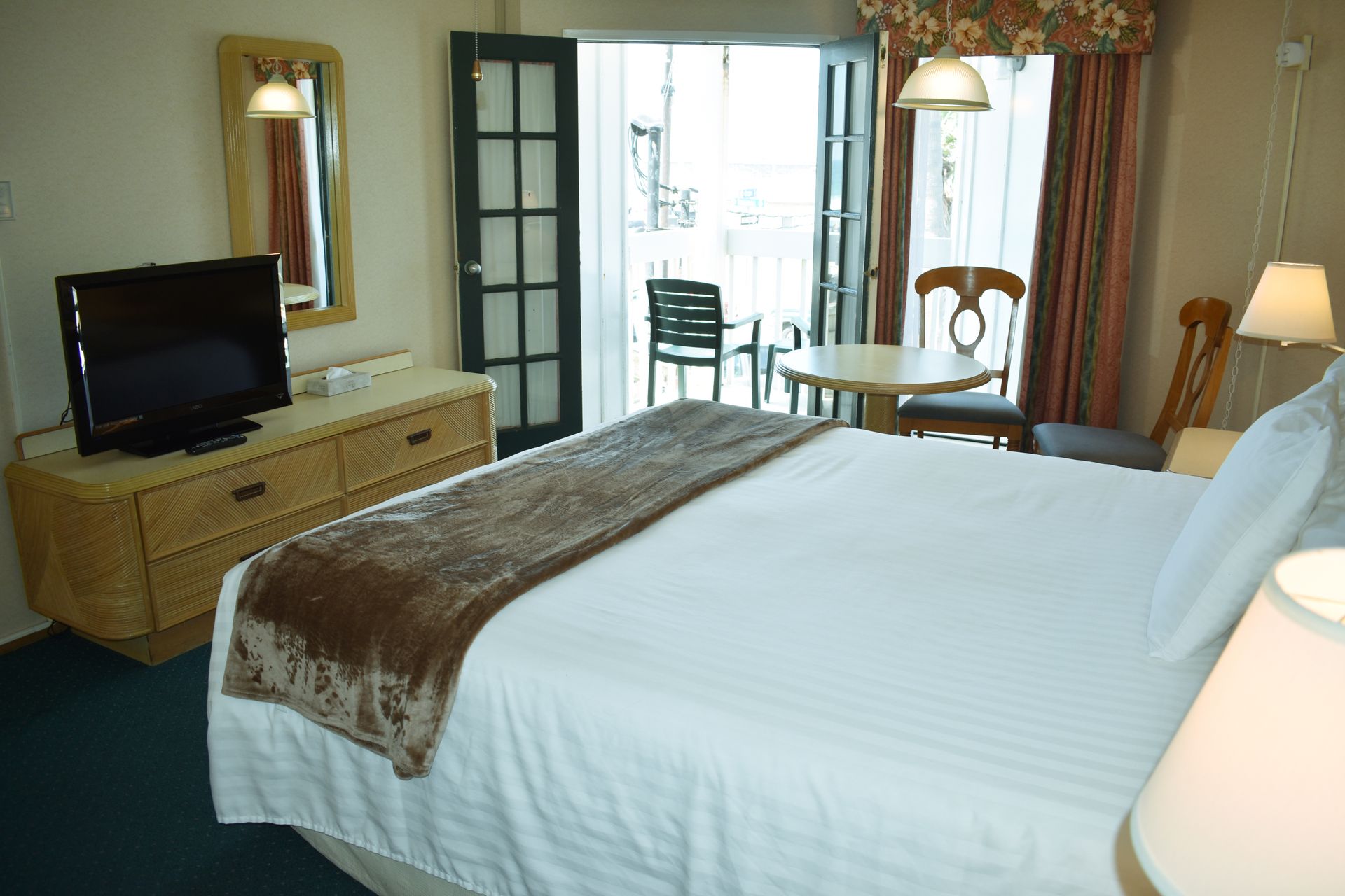 Hotel room with bed, dresser, TV, and balcony access.