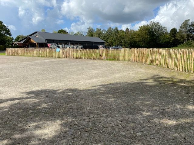 Een parkeerplaats met robinia hekwerk en een gebouw op de achtergrond.