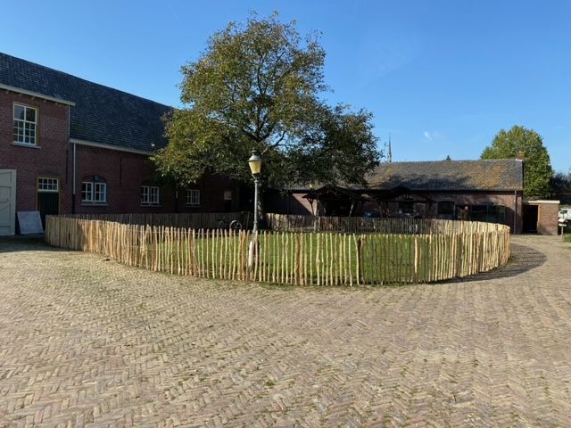 Een groot bakstenen gebouw met een robinia houten schapenhek ervoor.