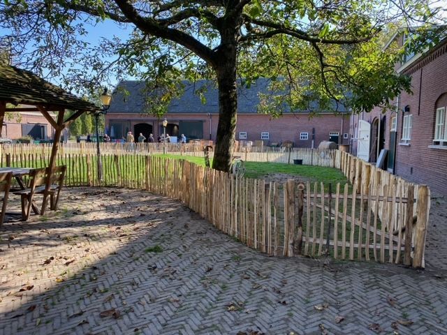 Een houten schapenhek van kastanje omringt een patio met een paard op de achtergrond.