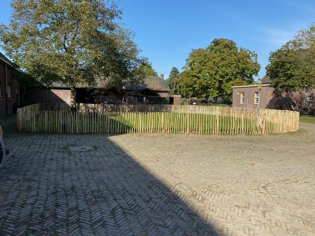 Een houten hek omringt een stenen oprit voor een gebouw.