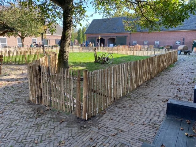 Een houten schapenhek omringt een stenen oprit voor een huis.