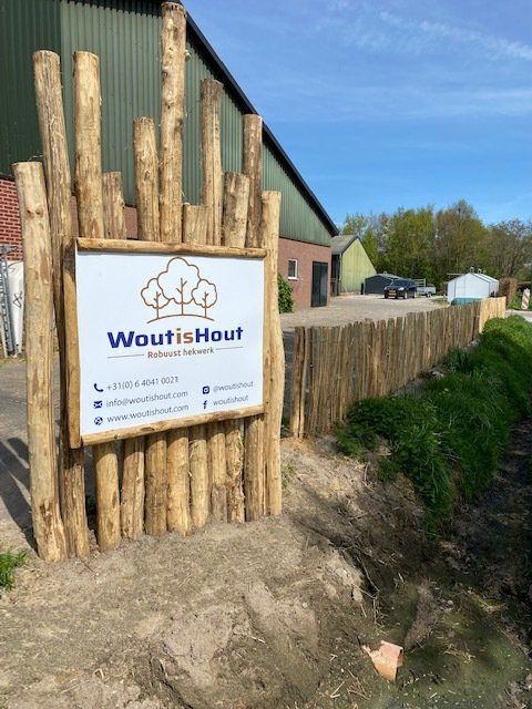 Een houten hek van robinia palen met een bordje woutishout.