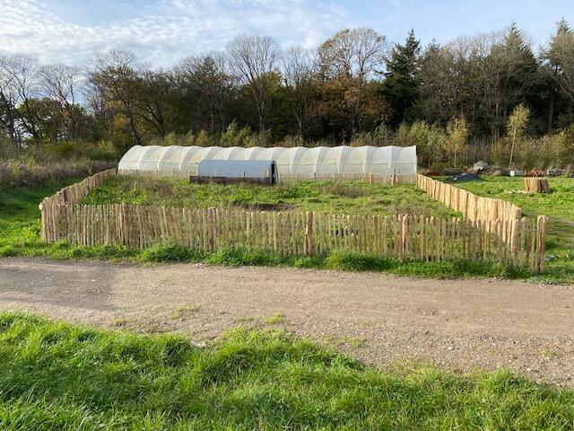 Een kas staat achter een houten schapenhek in een veld.
