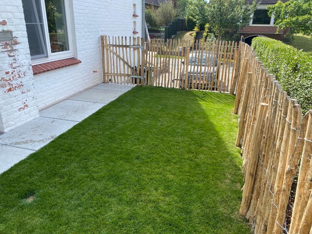 Een schapenhek van robiniahout omringt een weelderig groen gazon voor een wit bakstenen huis.