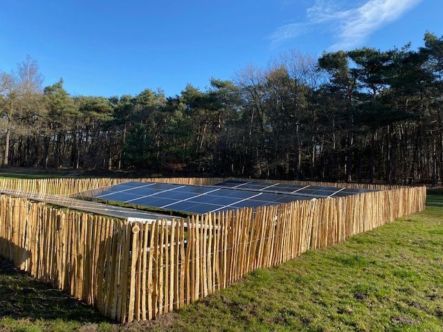 Een kastanje houten schapenhek met zonnepanelen erop in een veld.