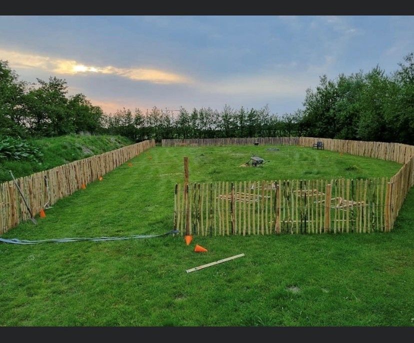 Een groot grasveld met een kastanje houten hek eromheen.